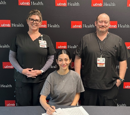 Image of man and woman standing next to woman sitting and signing papers