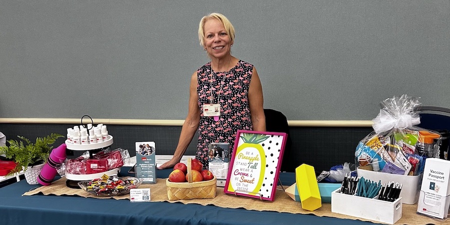 blonde, caucasian female standing behind a table adorned with back-to-school materials