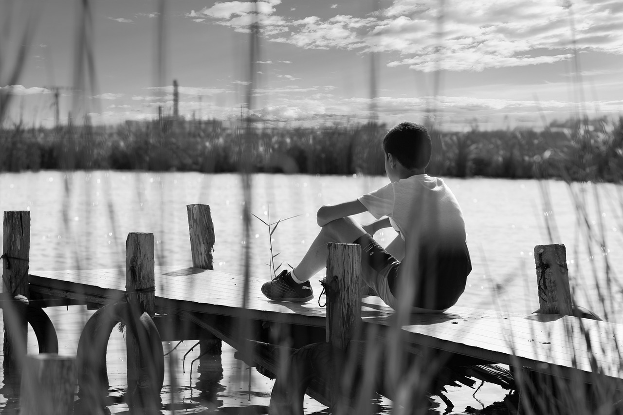 boy sitting on a dock near water