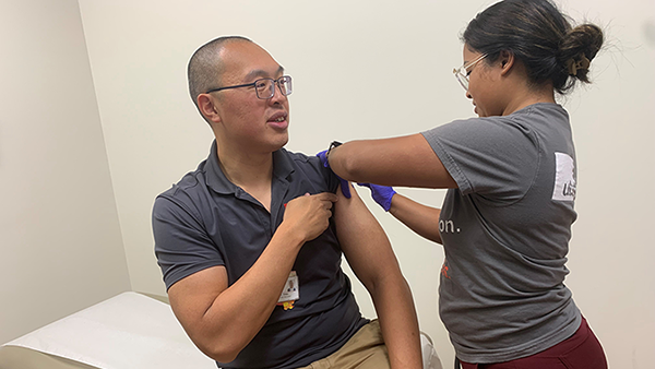 A man is rolling up his shirt sleeve to receive a flu shot from a female medical worker.