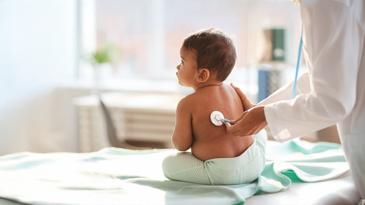 A baby is being examined by a medical provider who holds a stethoscope to his back